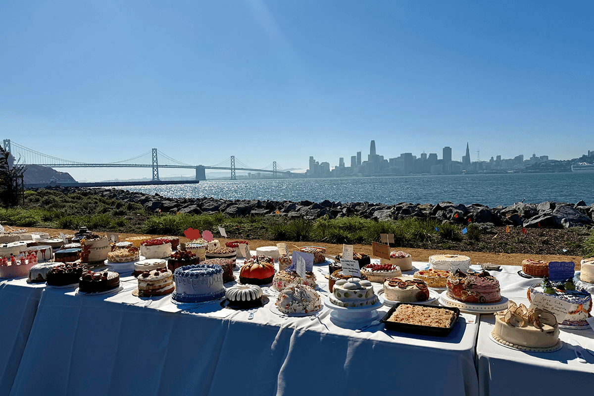 Dessert table with assorted cakes and pastries set along the Treasure Island waterfront overlooking the Bay Bridge and San Francisco skyline.