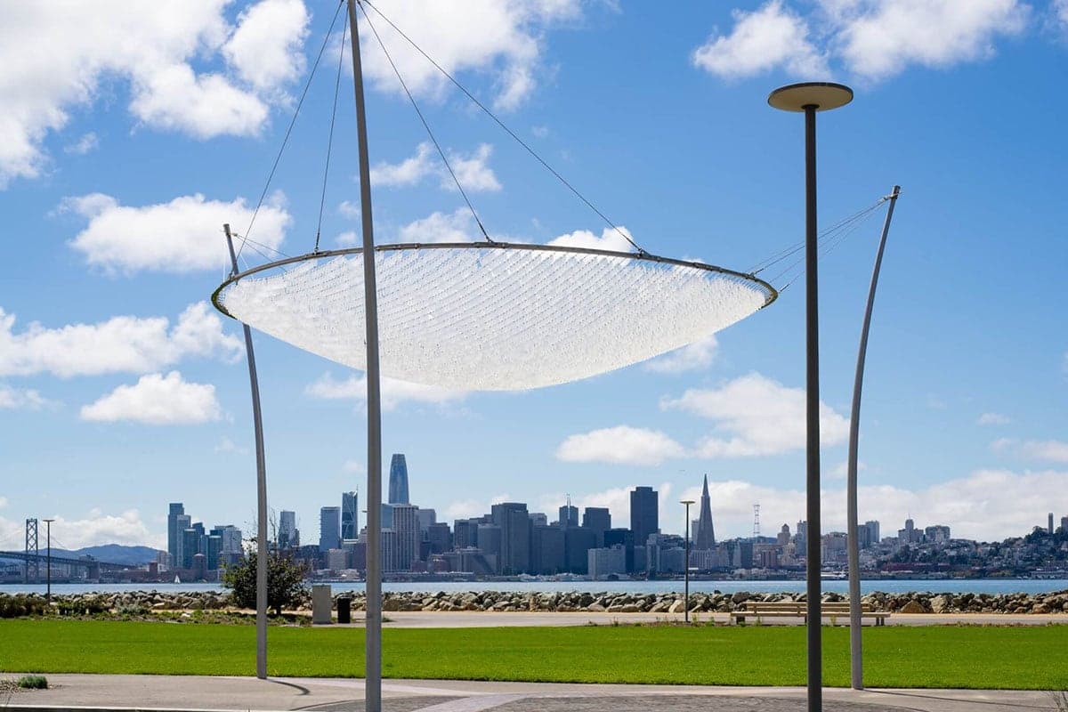 Modern shade canopy sculpture in a waterfront park on Treasure Island with the San Francisco skyline and Bay visible in the background.