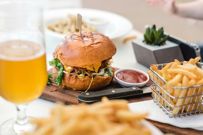 Gourmet cheeseburger with melted cheddar, fresh greens, and brioche bun served with crispy French fries, dipping sauce, and a glass of craft beer at Island Cove restaurant.