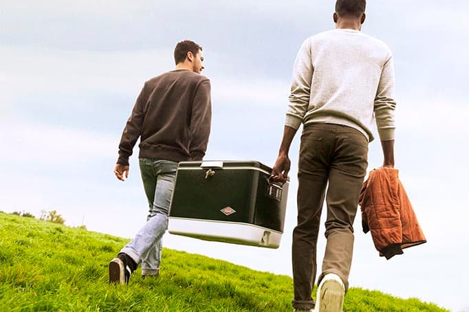 Two people carrying a cooler and jacket up a grassy hill at Signal Point Park.