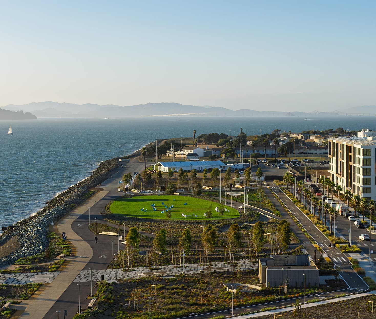 Elevated view of Treasure Island waterfront with shoreline paths, landscaped green space, and bay views stretching toward the horizon.