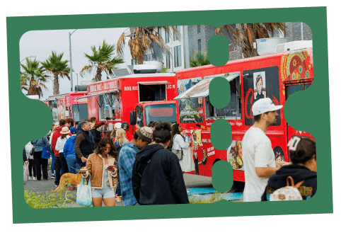 People lined up at colorful food trucks near palm trees at an outdoor event