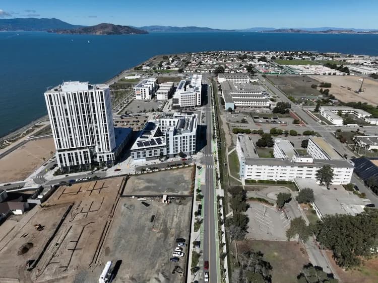 Aerial view of Treasure Island showing new residential towers, existing buildings, construction sites, and surrounding bay waters.