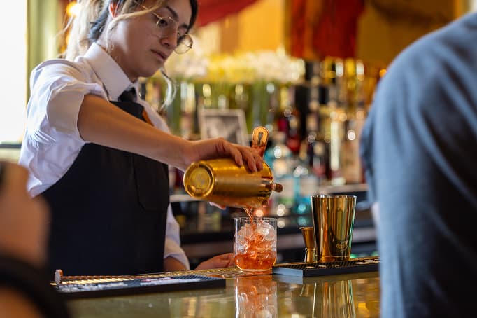 Bartender crafting a cocktail at a Treasure Island bar with polished brass tools and warm ambient lighting.