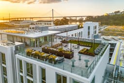 Rooftop terrace at a Treasure Island residential building with string lights, landscaped seating areas, and Bay Bridge views at sunset.