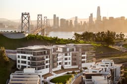 Modern Treasure Island condominiums at golden hour with the Bay Bridge and San Francisco skyline in the background.