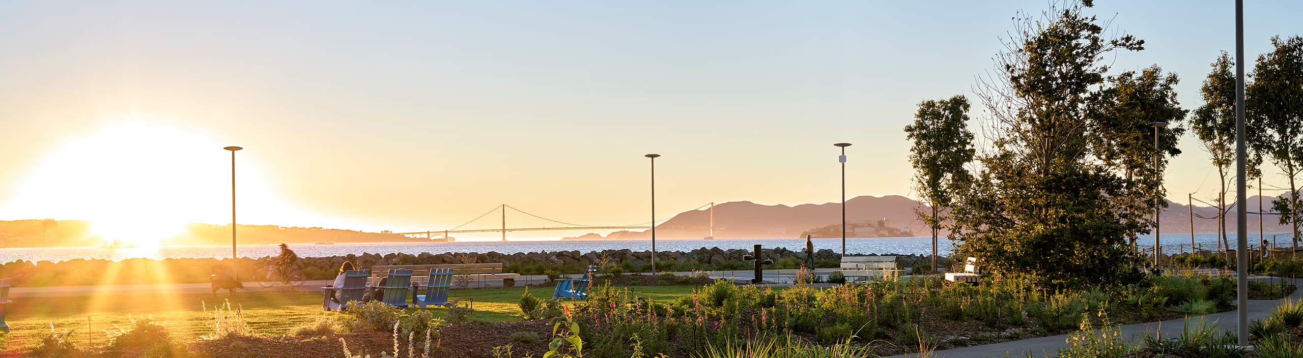 Sunset view from Cityside Park on Treasure Island with landscaped gardens, waterfront seating, and the Golden Gate Bridge visible across the bay.