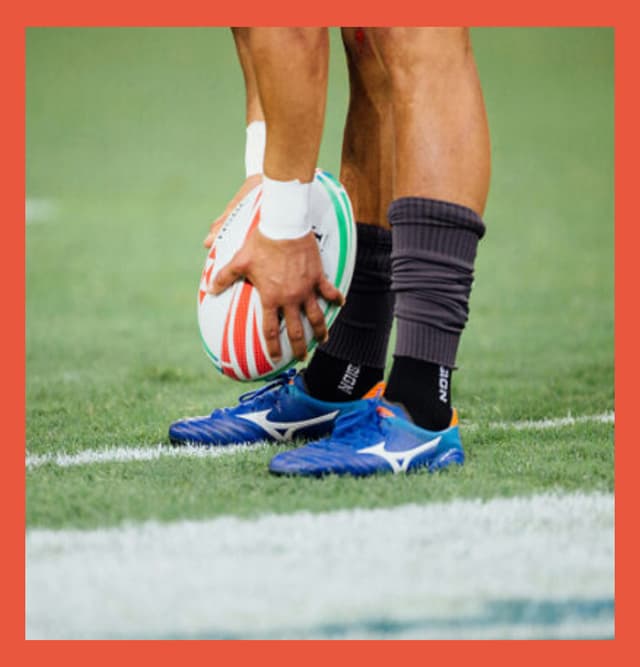 A close up of a man holding a rugby ball near his feet as if he were about to punt it at the San Francisco Gaelic Athletic Association