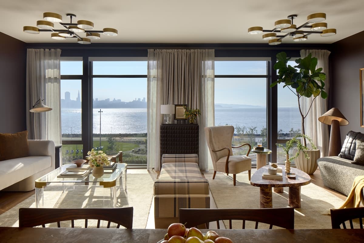 Elegant living room with expansive windows overlooking the bay and San Francisco skyline, featuring modern furnishings, abundant daylight, and scenic waterfront views.