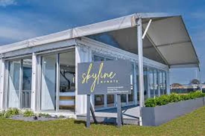 A modern white event pavilion with large windows and a canopy roof, set on a grassy lawn. A sign in front reads “Skyline Events,” indicating a waterfront event venue.